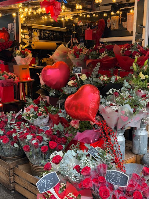 A vibrant display of floral arrangements featuring predominantly red and white roses, accented with green foliage and small white filler flowers, arranged in various bouquets and wrapped in tissue pap