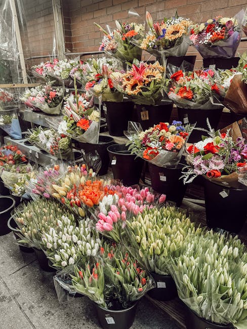 A display of fresh floral bouquets and bunches arranged in black buckets at a flower shop, featuring an array of tulips in various shades of pink, white, and red, alongside mixed flower arrangements i